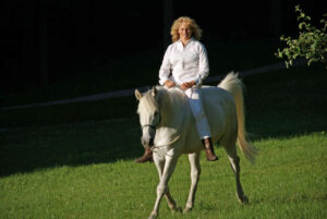 Ingrid Merkle und ihr Araber Pferd Schimmel traben auf einer Wiese mit Horsemanship am losen Zügel