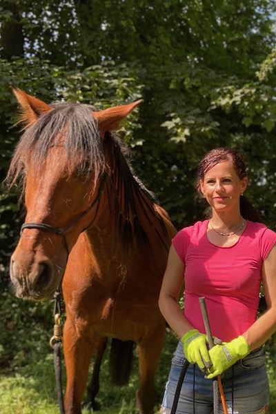 Alice Meutzner, Trainerin der Horsemanship mit ihrem braunen Pferd von vorne nebeneinander stehen.