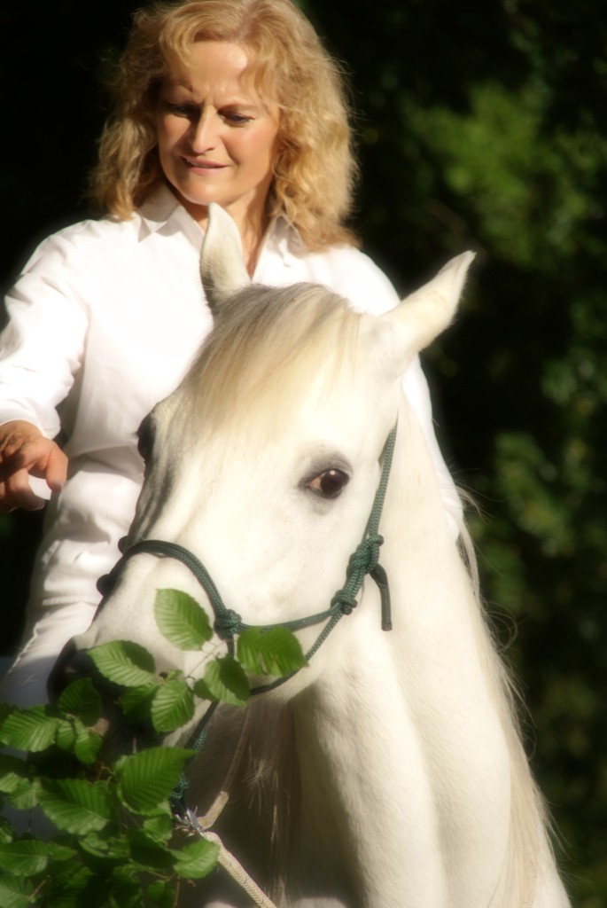 Ingrid Merkle sitzt auf ihrem Araber-Pferd Schimmel Radjib und zeigt auf einen Blätterzweig