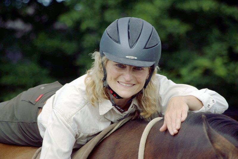 Horsemanship Wissen: eine Reiterin liegt auf einem braunen Pferd und lächelt in die Kamera